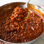 Baked beans with crispy bacon in a skillet, served warm and bubbly straight from the oven.