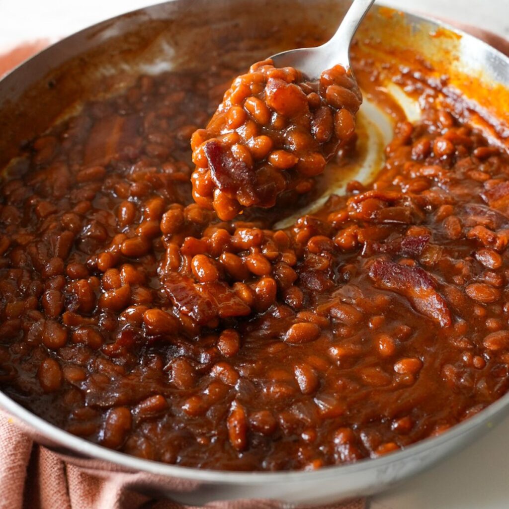 Baked beans with crispy bacon in a skillet, served warm and bubbly straight from the oven.