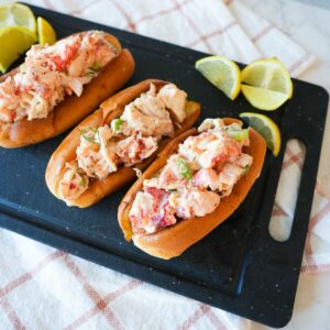 Lobster roll with creamy lobster salad in a toasted bun, garnished with herbs and lemon.