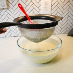 Straining Brazilian lemonade into a bowl.