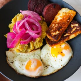Mangú con Los Tres Golpes, mashed plantains with fried salami, cheese, and eggs topped with onions.
