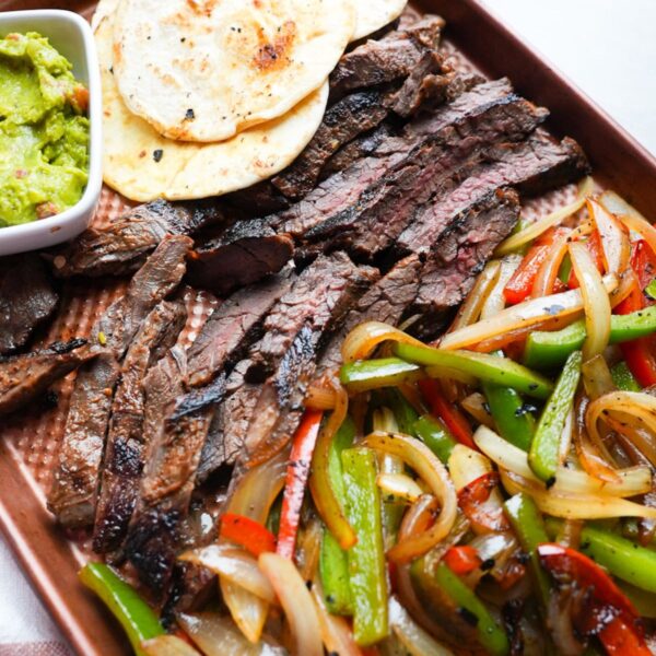 Steak fajitas on a sheet pan tray with tortillas and guacamole.