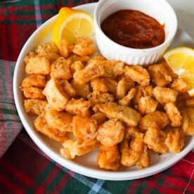 Golden, crispy calamari rings served with lemon wedges and marinara sauce on a white plate.