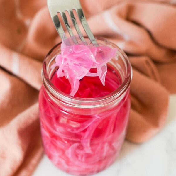 Pickled onions in a jar with some on a fork.