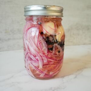 Red onions in a jar with vinegar, garlic & peppercorns.