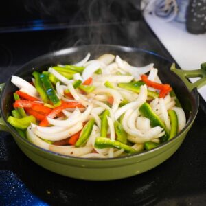 Onions and peppers cooking in a pan with steam.