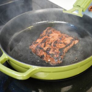 Skirt steak cooking in a cast iron pan.