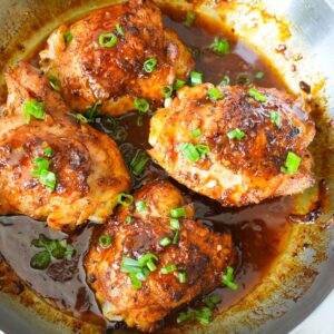 Crispy skin-on chicken thighs in a golden honey garlic glaze, garnished with green onions.