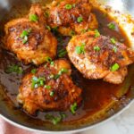 Crispy skin-on chicken thighs in a golden honey garlic glaze, garnished with green onions.