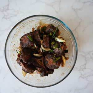 Oxtail marinating in a glass bowl with spices.