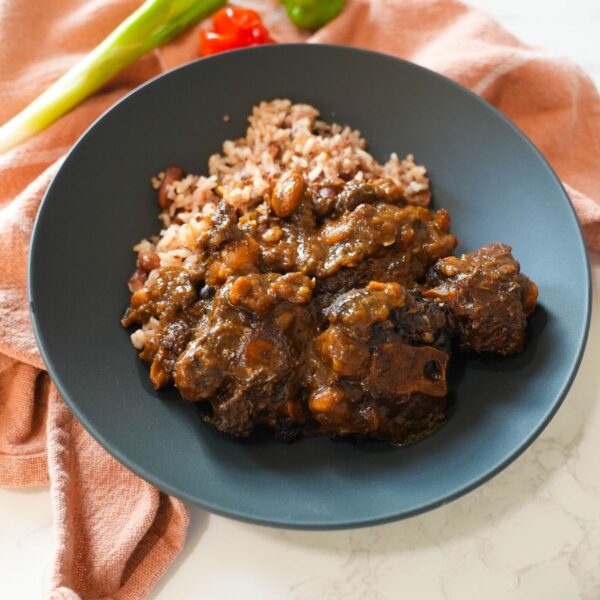 A bowl of Jamaican oxtail with thick gravy, butter beans, and herbs, served over steamed rice.