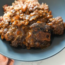 A bowl of Jamaican oxtail with thick gravy, butter beans, and herbs, served over steamed rice.