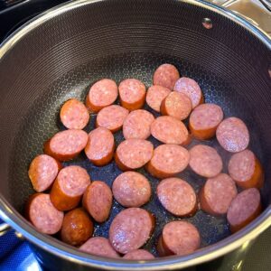 Sausage being browned in a pot.