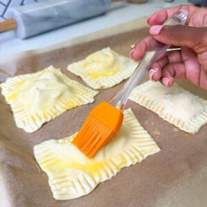 Egg wash being brushed on apple hand pies.