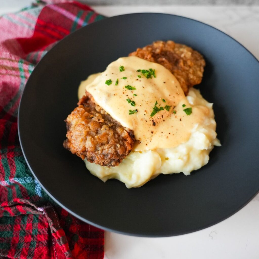 Golden chicken fried steak topped with creamy white gravy and chopped parsley, served with mashed potatoes.
