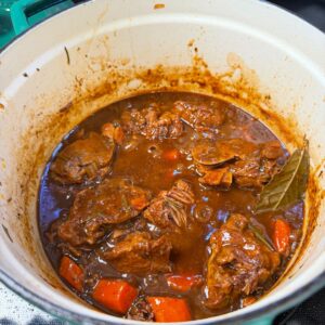 A pot of rich lamb stew with tender chunks of meat, carrots, and herbs in a dark, glossy broth.