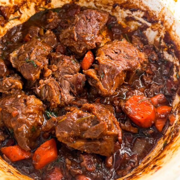 A pot of rich lamb stew with tender chunks of meat, carrots, and herbs in a dark, glossy broth.