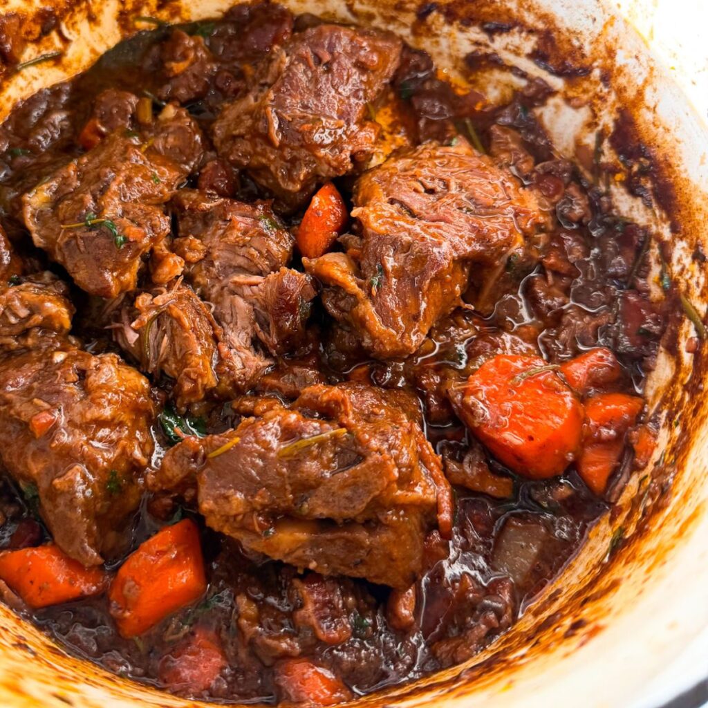 A pot of rich lamb stew with tender chunks of meat, carrots, and herbs in a dark, glossy broth.