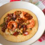Bowl of creamy cheddar grits topped with Cajun shrimp, crispy bacon, and a rich white wine butter sauce.