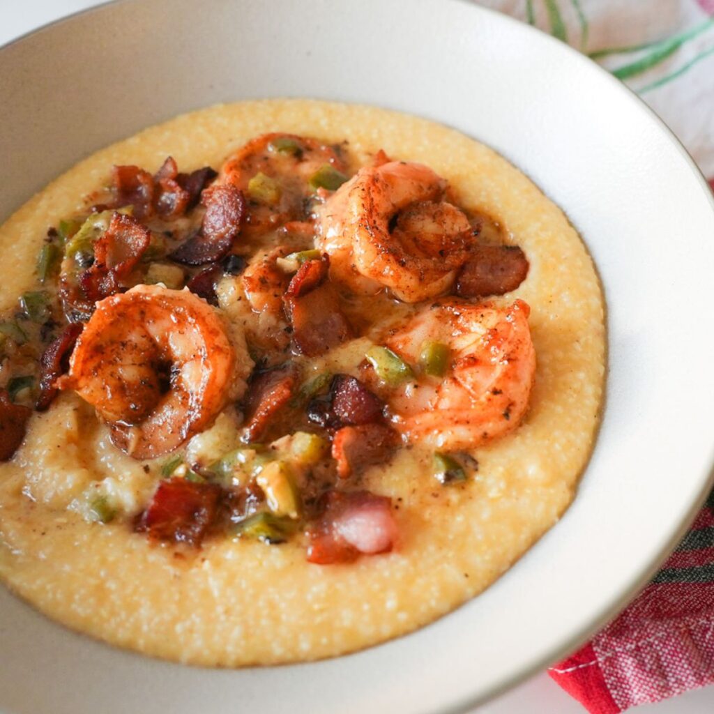 Bowl of creamy cheddar grits topped with Cajun shrimp, crispy bacon, and a rich white wine butter sauce.