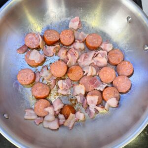 Sausage and bacon cooking in a pan.