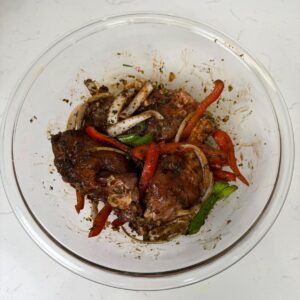 Chicken in a bowl with marinate, onions and peppers.