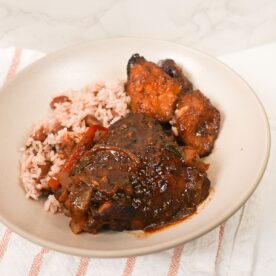 Brown stew chicken in thick brown gravy with sliced peppers, thyme, and rice and peas with plantain.