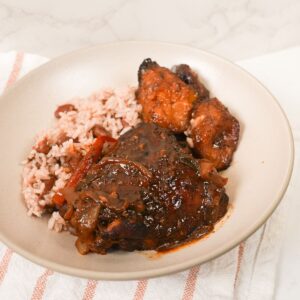 Brown stew chicken in thick brown gravy with sliced peppers, thyme, and rice and peas with plantain.