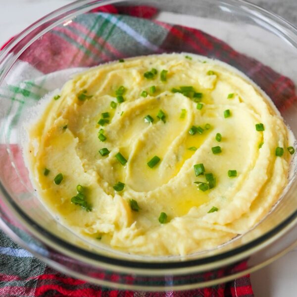 Mashed Yukon gold potatoes topped with melted butter and chopped chives, served in a glass bowl.