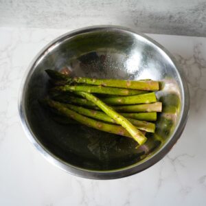 Asparagus in a silver bowl with salt and pepper.