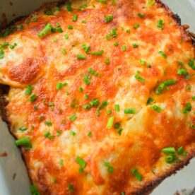 Cheesy scalloped potatoes baked in a small dish with golden brown melted cheese and chopped chives on top.