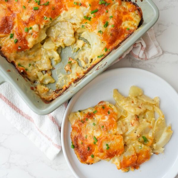 Cheesy scalloped potatoes in a small dish and some scooped onto a plate.