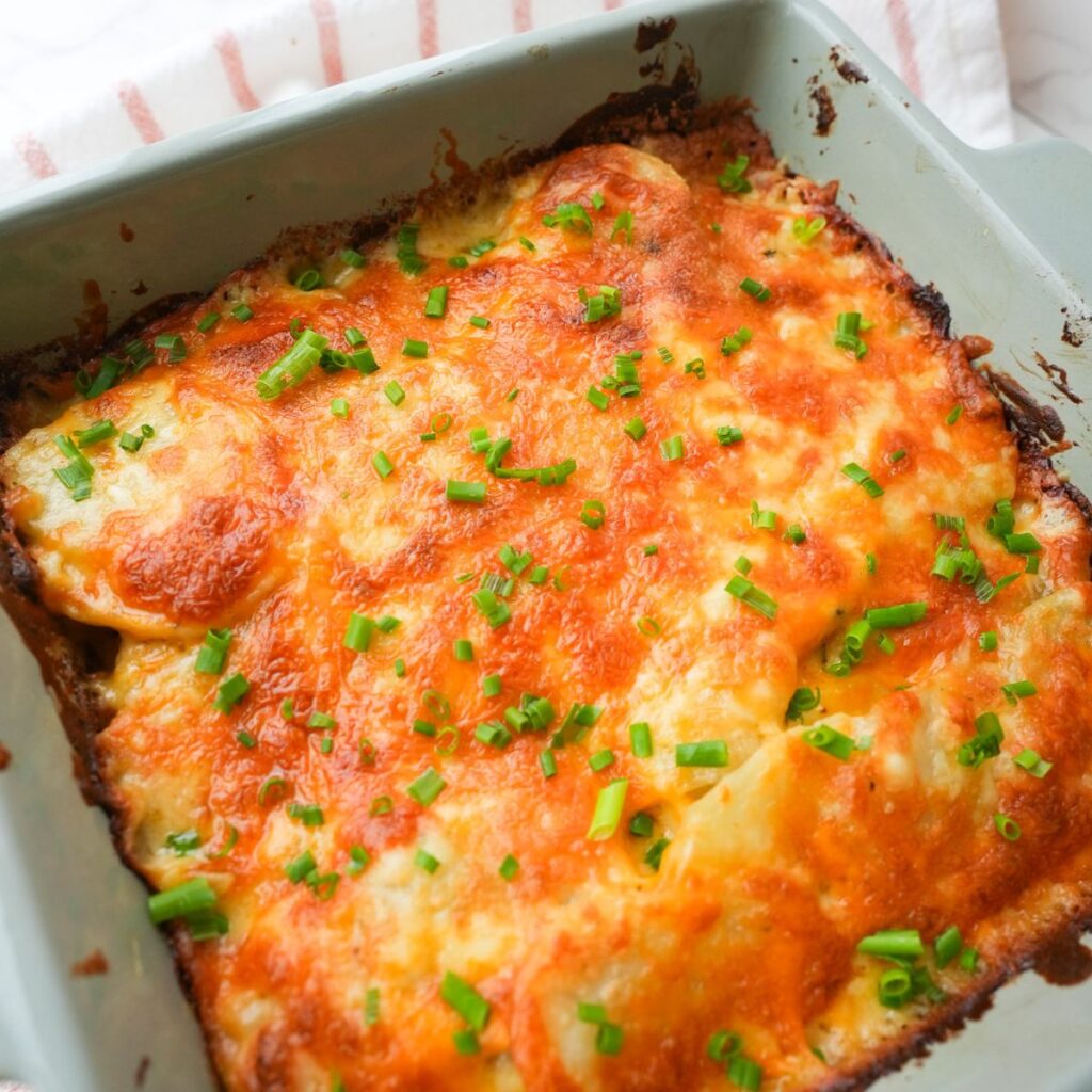 Cheesy scalloped potatoes baked in a small dish with golden brown melted cheese and chopped chives on top.