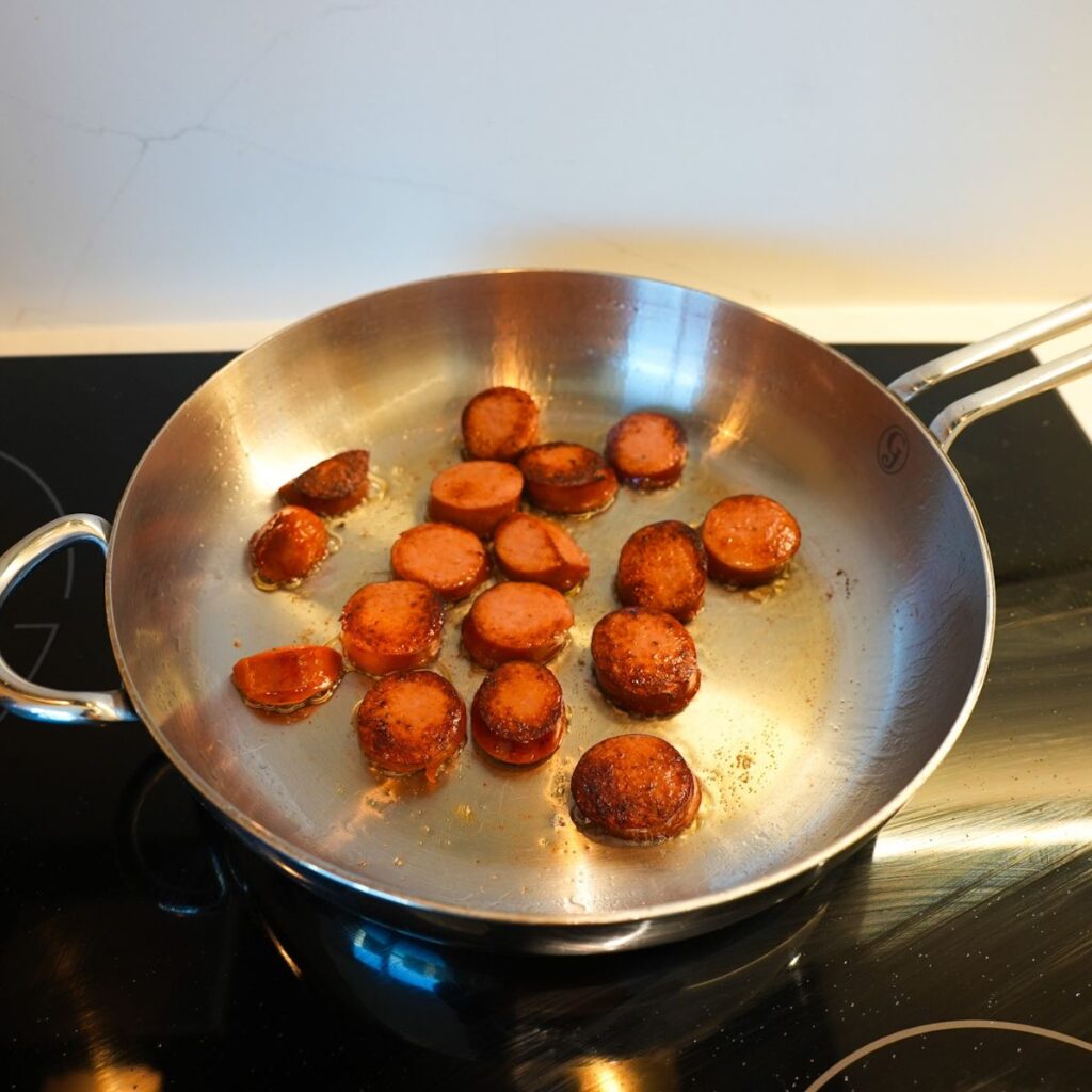 Smoked sausage being browned in a pan.