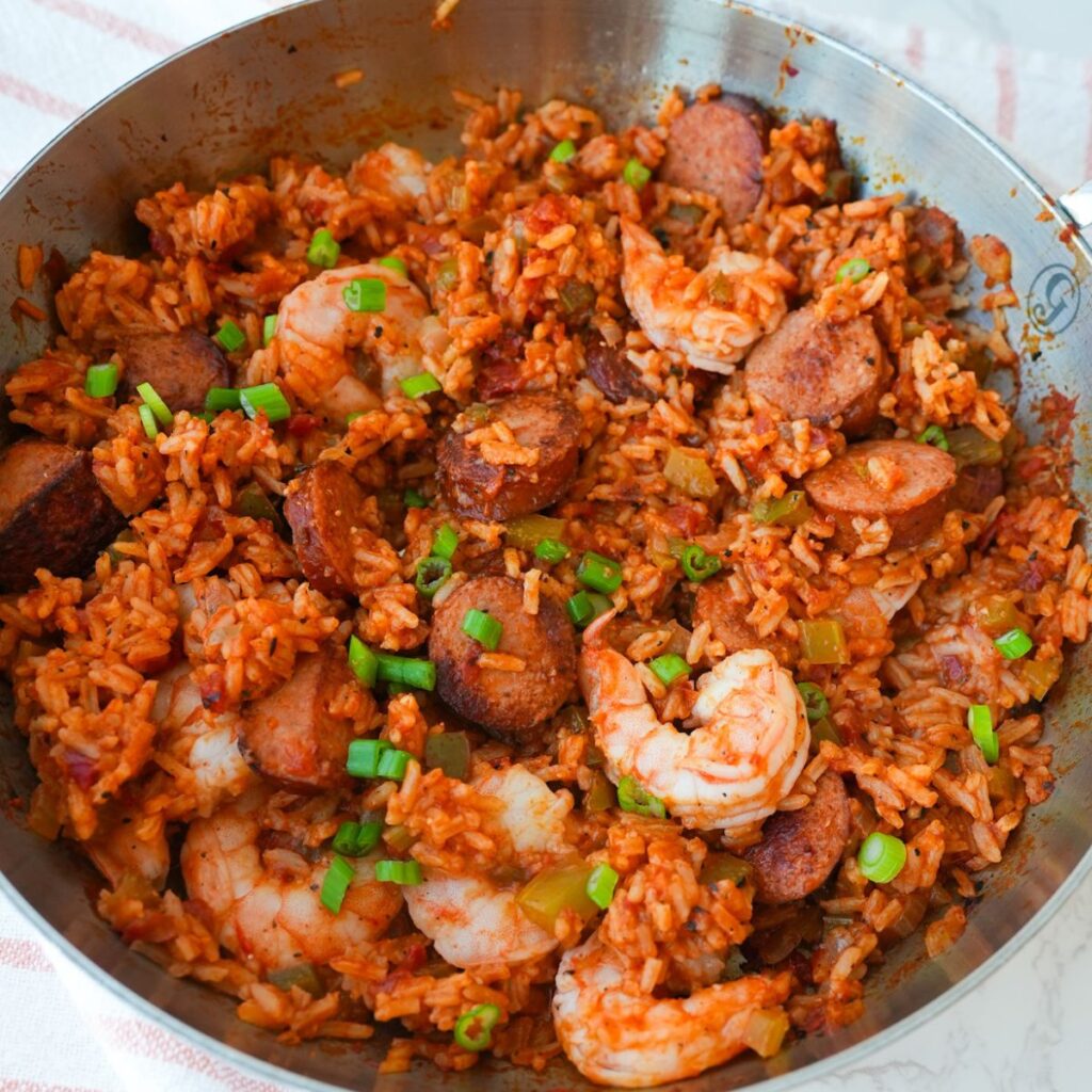Jambalaya in a skillet with shrimp, sliced sausage, rice, and chopped herbs on top.