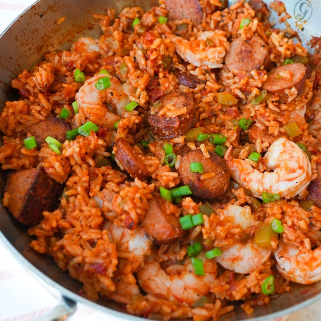Jambalaya in a skillet with shrimp, sliced sausage, rice, and chopped herbs on top.