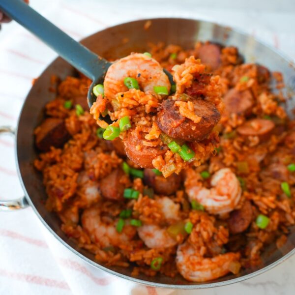 Jambalaya in a skillet with shrimp, sliced sausage, rice, and chopped herbs on top.