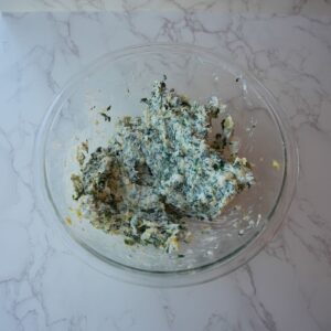 Spinach, artichokes, cream cheese and cheeses mixed up in a glass mixing bowl.