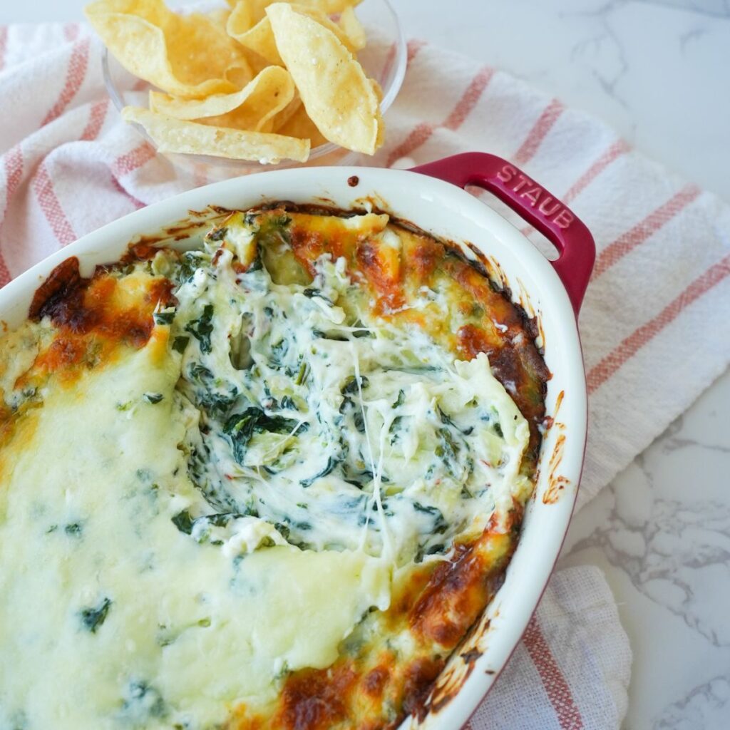 Cheesy spinach artichoke dip in a baking dish, served with tortilla chips.