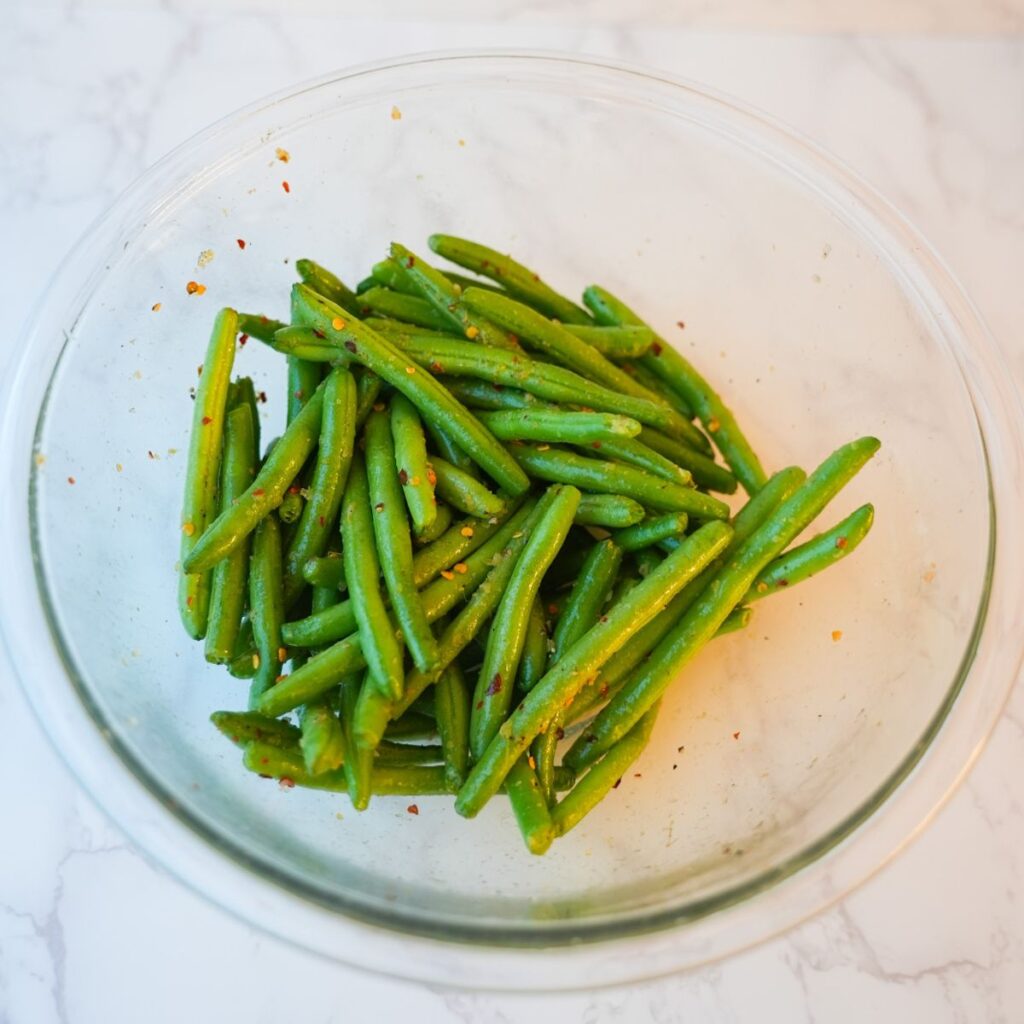 Green beans in a glass bowl with seasonings.