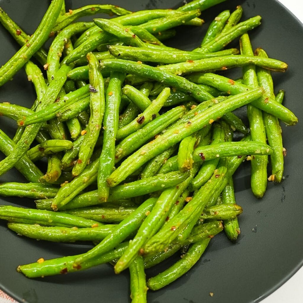 Air fryer green beans in a bowl with visible garlic, red pepper flakes, and lightly blistered edges.