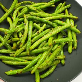 Air fryer green beans in a bowl with visible garlic, red pepper flakes, and lightly blistered edges.