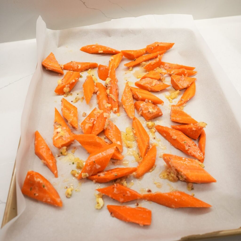 Carrots cut up with seasonings on a parchment lined baking sheet.