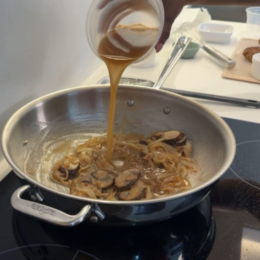 Broth being poured into pan with mushrooms and onions.