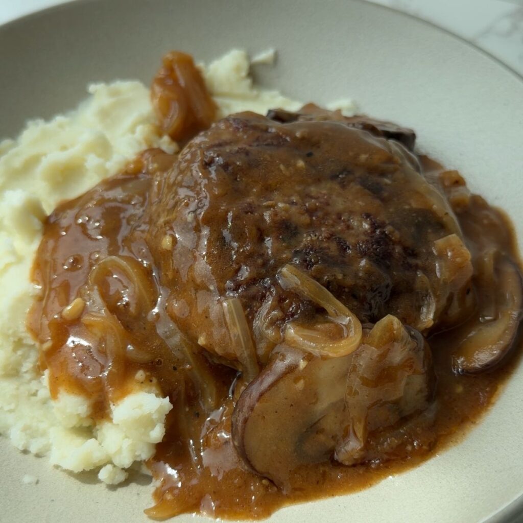 Salisbury steak patties in brown onion mushroom gravy, served over mashed potatoes.