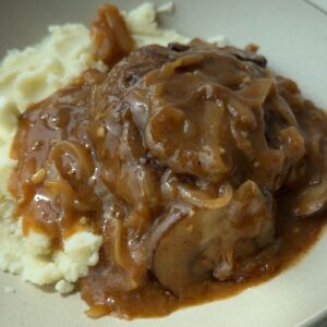 Salisbury steak patties in brown onion mushroom gravy, served over mashed potatoes.