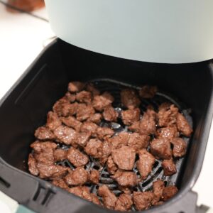 Steak bites in an air fryer basket.