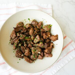 Air fryer steak bites in a bowl with garlic butter, browned edges, and chopped herbs on top.