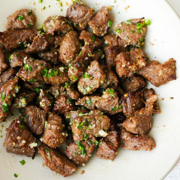 Air fryer steak bites in a bowl with garlic butter, browned edges, and chopped herbs on top.