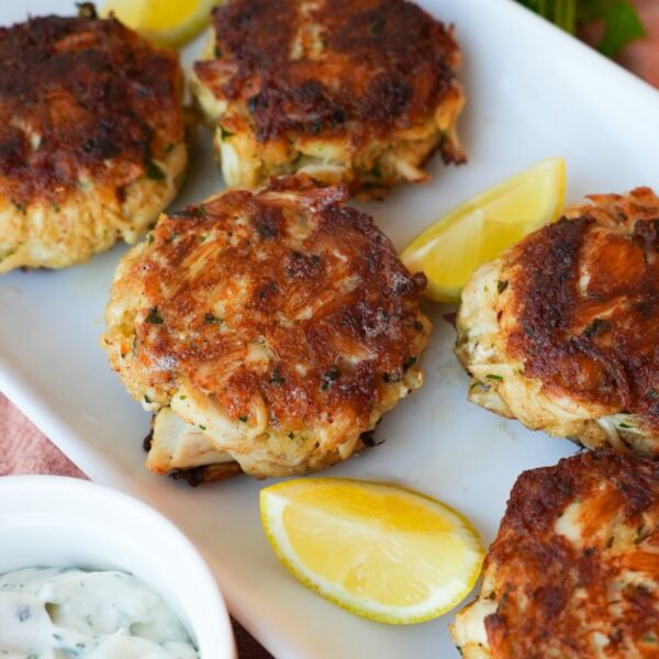 Golden crab cakes on a plate with crispy edges, fresh parsley, and a side of dipping sauce.